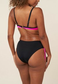 Ensemble de bikini noir comprenant un haut à bretelles avec des accents roses et un matériel ajustable, associé à un bas taille haute avec des nœuds sur les côtés.