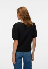 Zwarte, getextureerde top met korte, puffed mouwen en een ronde halslijn. Gepaard met high-waisted blauwe jeans, wat een casual stijl benadrukt.