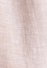 Tissu tissé beige présentant un motif de tissage serré et texturé avec des fils visibles et de légères irrégularités.