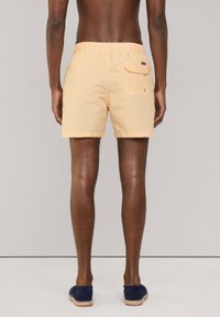 Shorts de bain rayés jaunes et blancs avec une ceinture élastique, une poche arrière et une coupe décontractée, associés à des espadrilles bleues.