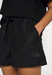 Shorts noirs avec une taille élastique et un cordon de serrage, dotés de poches avant et d'un logo discret sur l'ourlet. Texture de tissu lisse.