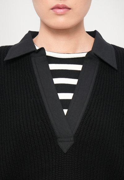 Black textured top with a V-shaped collar, layered over a black and white striped shirt. The collar is flat and pointed, contrasting the patterns below.