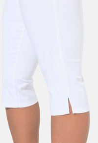 Leggings bianchi a vita alta con texture liscia, design aderente e un sottile dettaglio a spacco all'orlo, che enfatizzano una silhouette elegante.