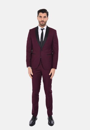 Abito bordeaux con rever in satin nero, camicia bianca e cravatta nera. Vestibilità su misura e taglio slim. Scarpe in pelle nere completano il look.