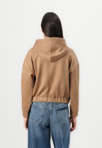 Haut de sweat à capuche court marron avec un cordon de serrage et un ourlet élastiqué, fabriqué en tissu doux. Porté avec un jean taille haute bleu.