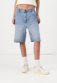 Ljusblå denimshorts med rak skärning, som har en femfickdesign och en midja med knappstängning. Bärs med vita sneakers.
