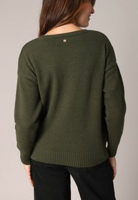 Olijfgroen gebreid sweater met een losse pasvorm, geribbelde zoom en een kleine accentknop aan de achterkant. Zachte textuur en brede mouwen.