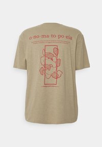 Beige bomulds t-shirt med korte ærmer. Rød grafisk tekst og abstrakte former trykt på ryggen, med ordet "onomatopoeia."