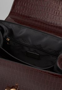 Burgundy faux-krokodilskinn handväska med svart tyginteriör, har en dragkedjeficka och detaljer i guldton.