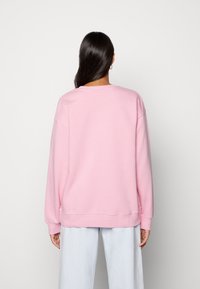 Rosa oversized sweatshirts med rund halsringning, sänkta axlar och ribbade ärmslut. Mjukt tyg med en slät struktur, bärs med ljusblå byxor.