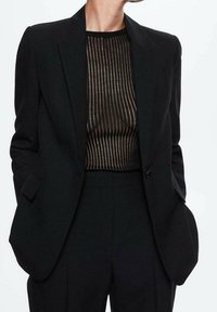 Sorte skræddersyet blazer med en struktureret design, parret med en gennemsigtig, stribet top med vandrette linjer i varierende nuancer.