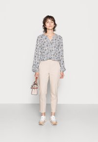 Blusa de manga longa com um padrão floral azul e branco, combinada com calças bejes ajustadas, sapatilhas brancas e uma pequena bolsa rosa.