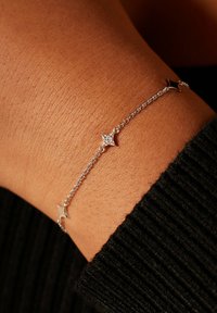 Zilveren armband met een fijne ketting en drie stervormige accenten, waarvan één versierd met kleine steentjes, getoond op een getextureerd huidoppervlak.
