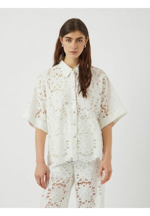 Camisa de encaje blanca con patrones florales, mangas cortas y cierre de botones. Detalles intrincados y tejido ligero. Combinada con pantalones a juego.