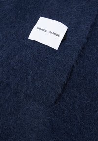 Mørkeblå ullblandingsstoff med en myk, strukturert overflate; har et hvitt merkelapp med teksten "SAM SøE SAM SøE" trykt i svart.