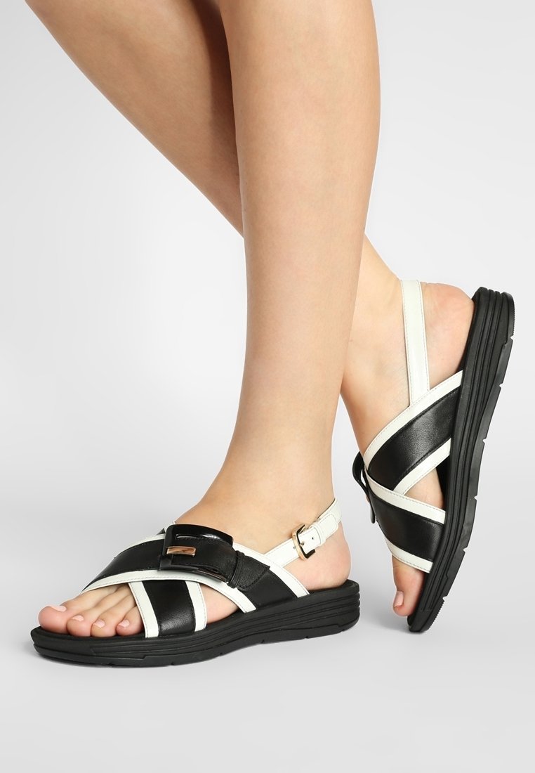 Mustavalkoiset nahka sandaalit, joissa on ristikkäiset remmit, solk yksityiskohta ja teksturoitu musta pohja; avonainen varvaspäällinen ja säädettävä nilkkaremmi.