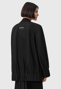 Giubbotto bomber nero con vestibilità rilassata, polsini e orlo elasticizzati. Presenta un'etichetta quadrata sul retro con il testo "ALLSAINTS". Tessuto morbido.