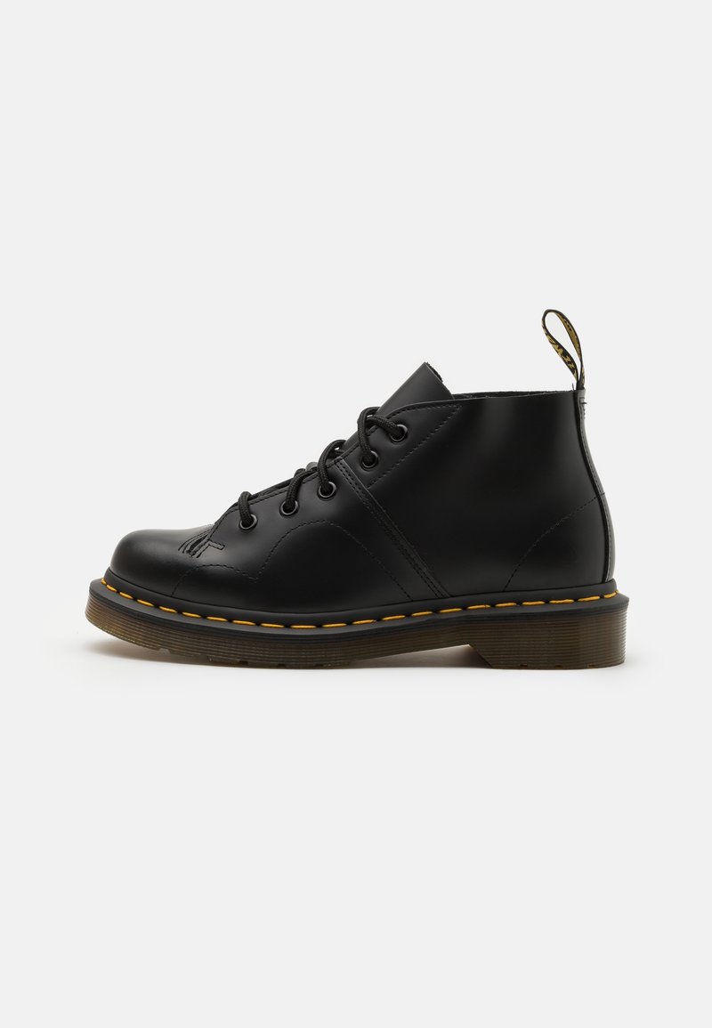 Bottes en cuir noir à la cheville avec un bout rond, un design à lacets, des détails de couture jaune, et une semelle en caoutchouc durable.