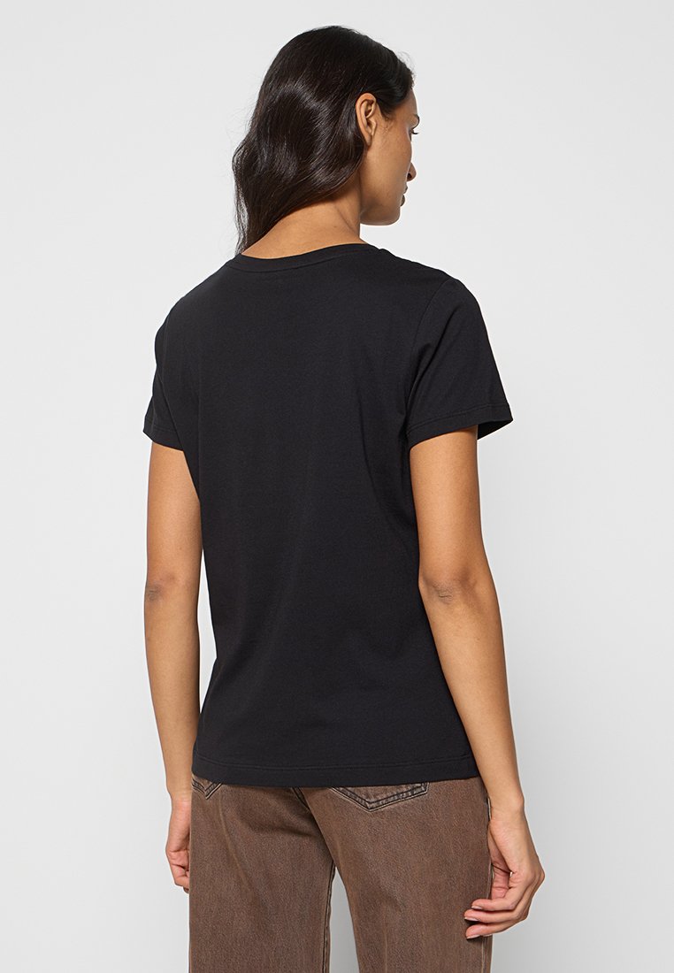 Czarna bawełniana koszulka z okrągłym dekoltem i krótkimi rękawami, o prostym kroju i gładkiej fakturze, noszona z brązowymi spodniami.