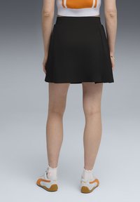 Jupe plissée noire au toucher lisse, assortie à des baskets blanches avec des accents orange. Fini mat, design mi-long.