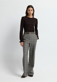Top marrón de manga larga con un cuello fruncido y detalle de botones, combinado con pantalones de cuadros de cintura alta en tonos grises y marrones.