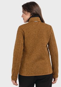 Braune, strukturierte Fleecejacke mit hohem Kragen, kontrastierender schwarzer Fütterung und dekorativer Stickerei an den Seiten.