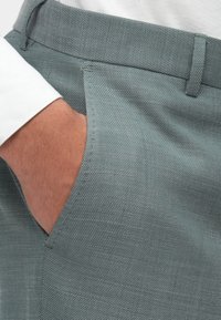 Pelēki zili bikses ar teksturētu audumu, ar sānu kabatu un gludu jostu. Šuvju kvalitāte ir laba un taisna.