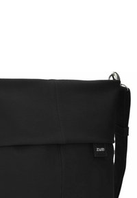 Borsa a tracolla in pelle nera con una superficie liscia, patta ripiegabile, tracolla regolabile e un piccolo etichetta del marchio sulla parte anteriore.