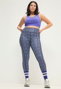 Paarse sportieve crop top gecombineerd met hoge tailleleggings met een blauw bloemenpatroon en contrasterende zwarte naden.