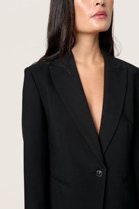 Černý blejzr s hlubokým výstřihem do V, klopami a jedním knoflíkem. Vyrobeno z hladkého materiálu, s přiléhavým střihem a prošitými detaily.