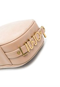 Borsa rotonda beige realizzata in pelle e tessuto testurizzato. Presenta un logo metallic oro e dettagli hardware sulla tracolla. Superficie liscia con accenti minimi.