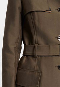 Bruine trenchcoat met een ceintuur in de taille, schouderflappen en twee voorzakken. Heeft een knoopsluiting en glanzende hardwareaccenten.