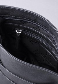 Black leather handbag interior featuring multiple pockets, zip closures, and patterned fabric lining with a smooth texture and sturdy stitching.