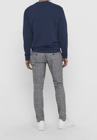 Granatowy sweter z okrągłym dekoltem w połączeniu z szarymi spodniami w kratę, o dopasowanym kroju i dwóch tylnych kieszeniach, noszony z białymi sneakersami.