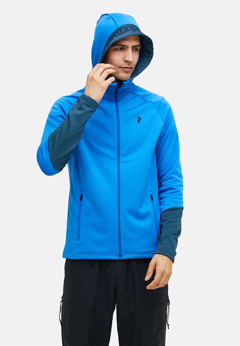 Giacca blu con cappuccio, dotata di una cerniera full zip, maniche di un blu scuro a contrasto, due tasche con zip e logo sul petto e all'interno del cappuccio.