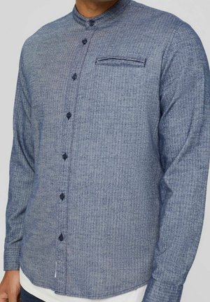 Herre blå tekstureret langærmet skjorte med båndkrave, knaplukning foran og brystlomme, båret over et hvidt stykke tøj.