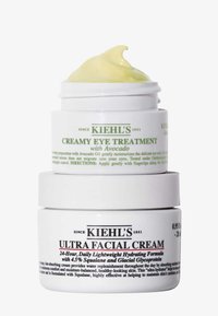 Il set di barattoli Kiehl's presenta un design in plastica bianca. Il barattolo superiore contiene una crema gialla; il barattolo inferiore, una crema bianca con testo e decorazioni nere.