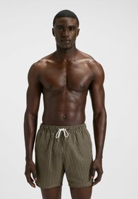 Braune Badehose mit vertikalen schwarzen Streifen, ausgestattet mit einem elastischen Bund und weißem Kordelzug. Glattes Material, knielange Schnittform.
