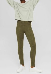 Jasnozielony krótki sweatshirt w połączeniu z oliwkowymi zamszowymi legginsami. Legginsy mają wysoki stan i gładką teksturę. Bia�łe sneakersy dopełniają stylizację.