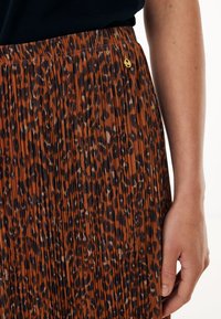 Jupe plissée imprimée léopard dans des tons marron et noir, avec un accent de logo doré et une taille élastique. La texture semble lisse et fluide.