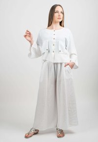Vit linne tvådelad outfit med en cropped topp som har knappar och vida byxor, båda med en mjuk textur och sidofickor.