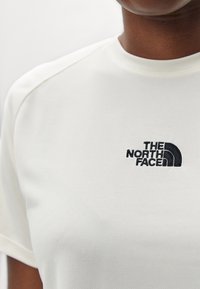 Vit kortärmad skjorta i strukturerad tyg, med en svart broderad logotyp av "The North Face" på vänster bröstområde.