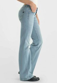 Jeans en denim bleu clair avec une coupe droite, poches avec des détails de couture et une finition légèrement délavée. Chaussures noires portées avec les jeans.