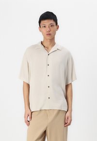 Beige short-sleeve shirt with a relaxed fit, button-up front, and a notch collar. Smooth fabric with brown buttons and no visible patterns.