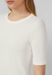 T-shirt blanc côtelé avec un col rond et des manches courtes, présentant une texture lisse et un design ajusté.