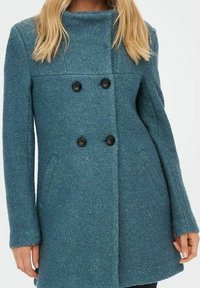 Cappotto doppiopetto in tessuto teal texture con colletto alto e due bottoni neri; presenta tasche laterali e una linea dritta.