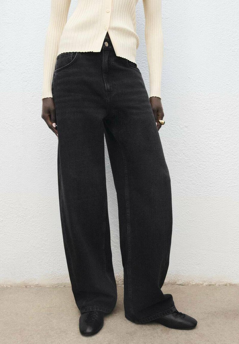 Zwarte denimbroek met wijde pijpen en hoge taille, vijf zakken en subtiele vervaging. Gecombineerd met een crèmekleurige geribde cardigan.