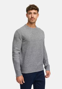 Grijze gebreide trui met geribbelde manchetten en zoom, gemaakt van zacht materiaal, gecombineerd met donkerblauwe jeans. Ronde halsontwerp met een gestructureerde afwerking.