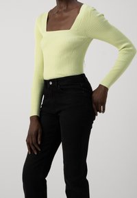 Top de manga larga acanalado en verde claro con escote cuadrado, combinado con jeans negros. El top cuenta con una tela texturizada y un diseño ajustado.