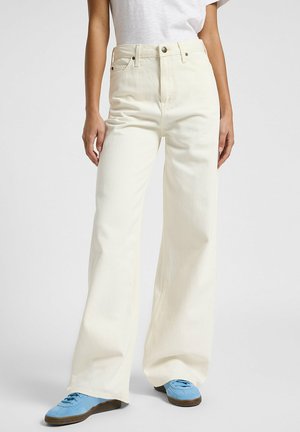 Jeans wide-leg en denim blanc cassé. Taille haute, avec poches avant, couture discrète, et associés à des baskets bleu clair.